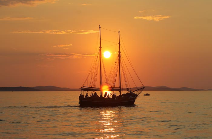Un barco de vela pasar por delante del sol durante el atardecer en Zadar